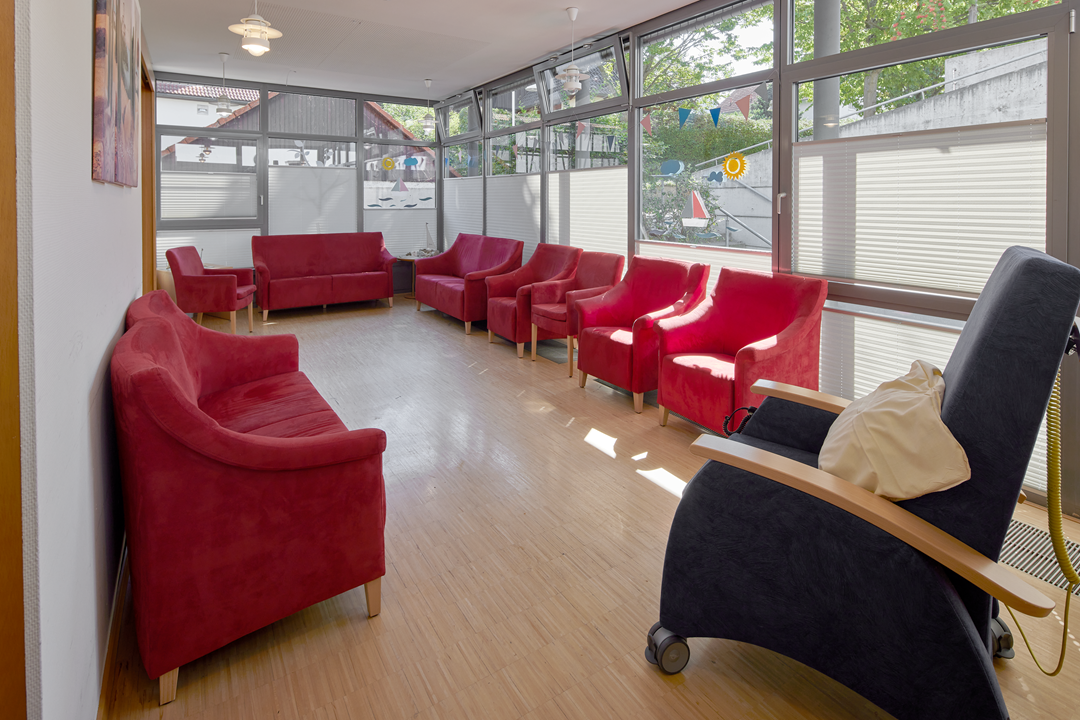 Gemütlicher Wartebereich mit roten Sesseln und Sofa.