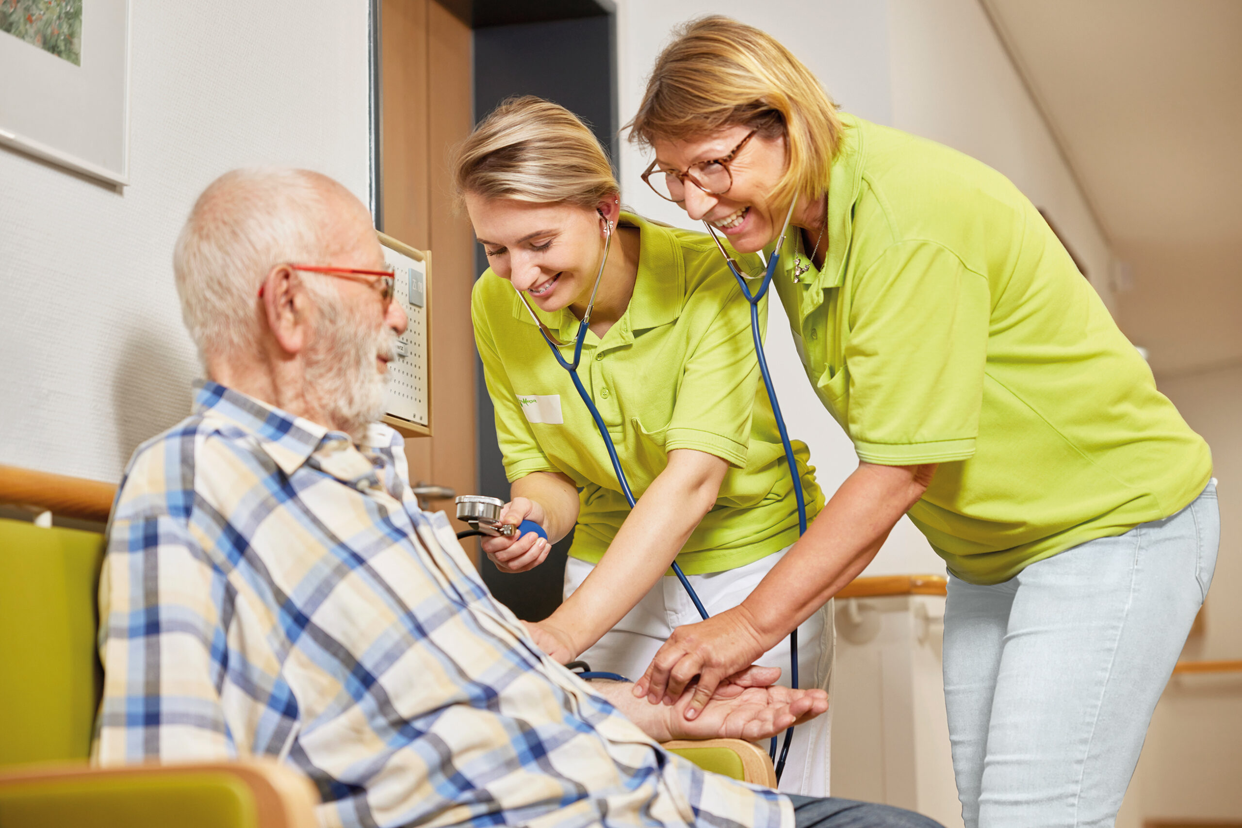 Zwei Pfleger untersuchen älteren Mann im Rollstuhl.