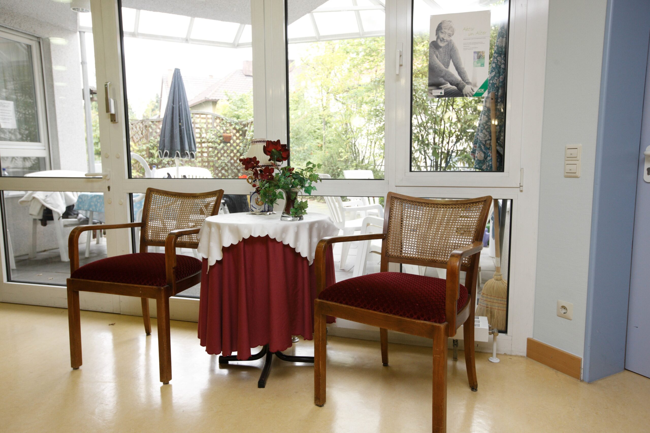 Zwei Stühle, Tisch mit Blumen, helle Fensterfront.
