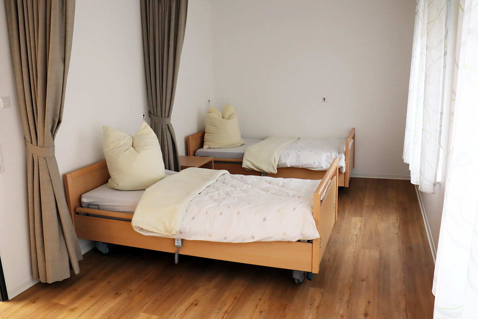 Zwei Betten in hellem Zimmer mit Holzfußboden.