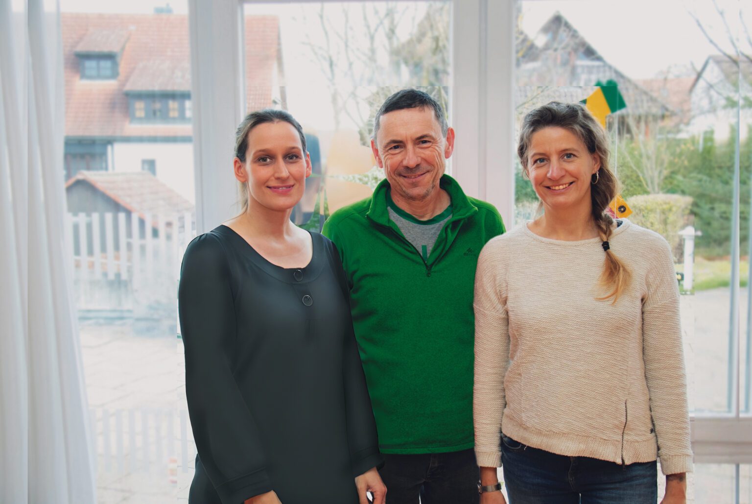 Drei Personen lächeln vor einem Fenster