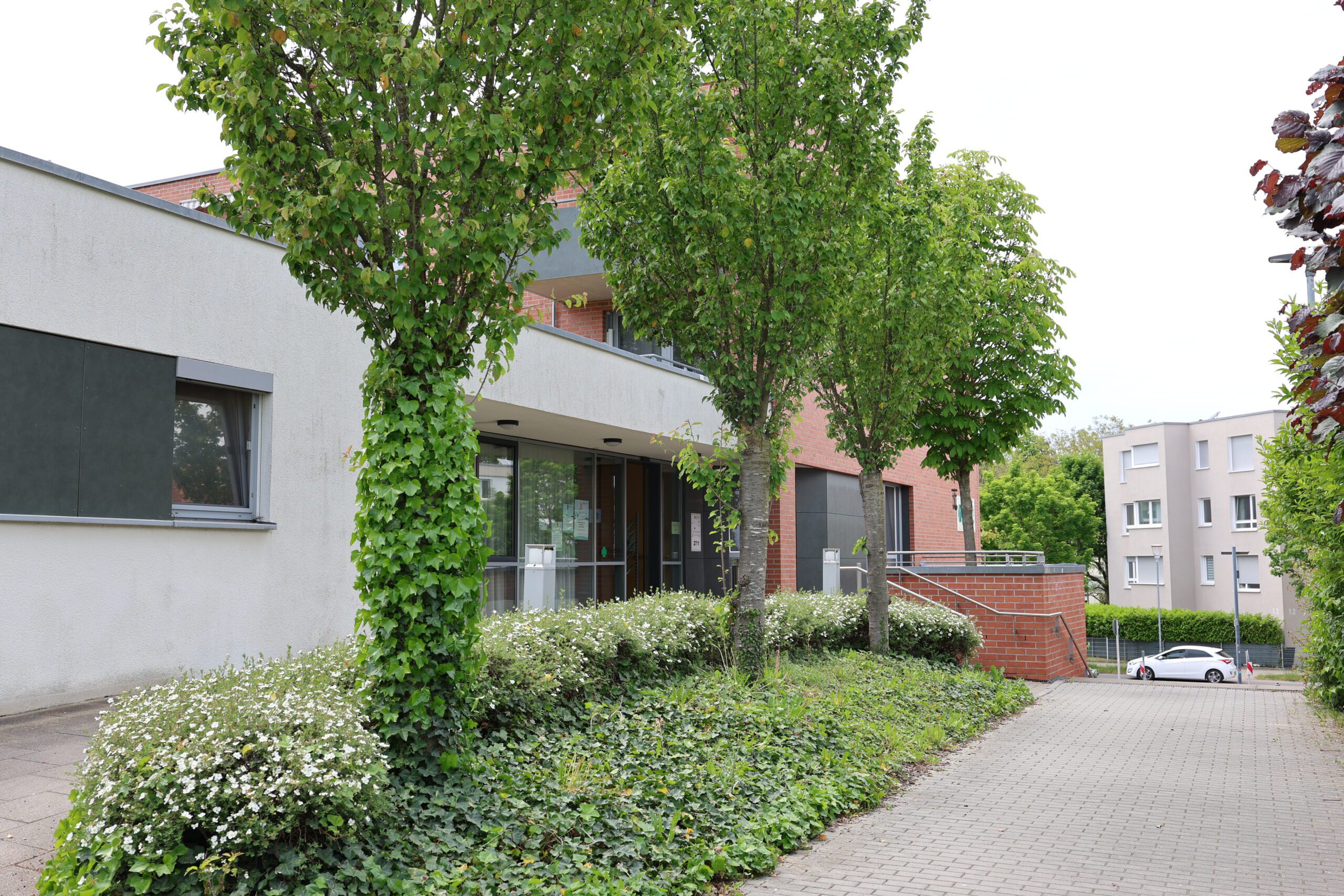 Gehweg vor modernem Gebäude mit Bäumen.