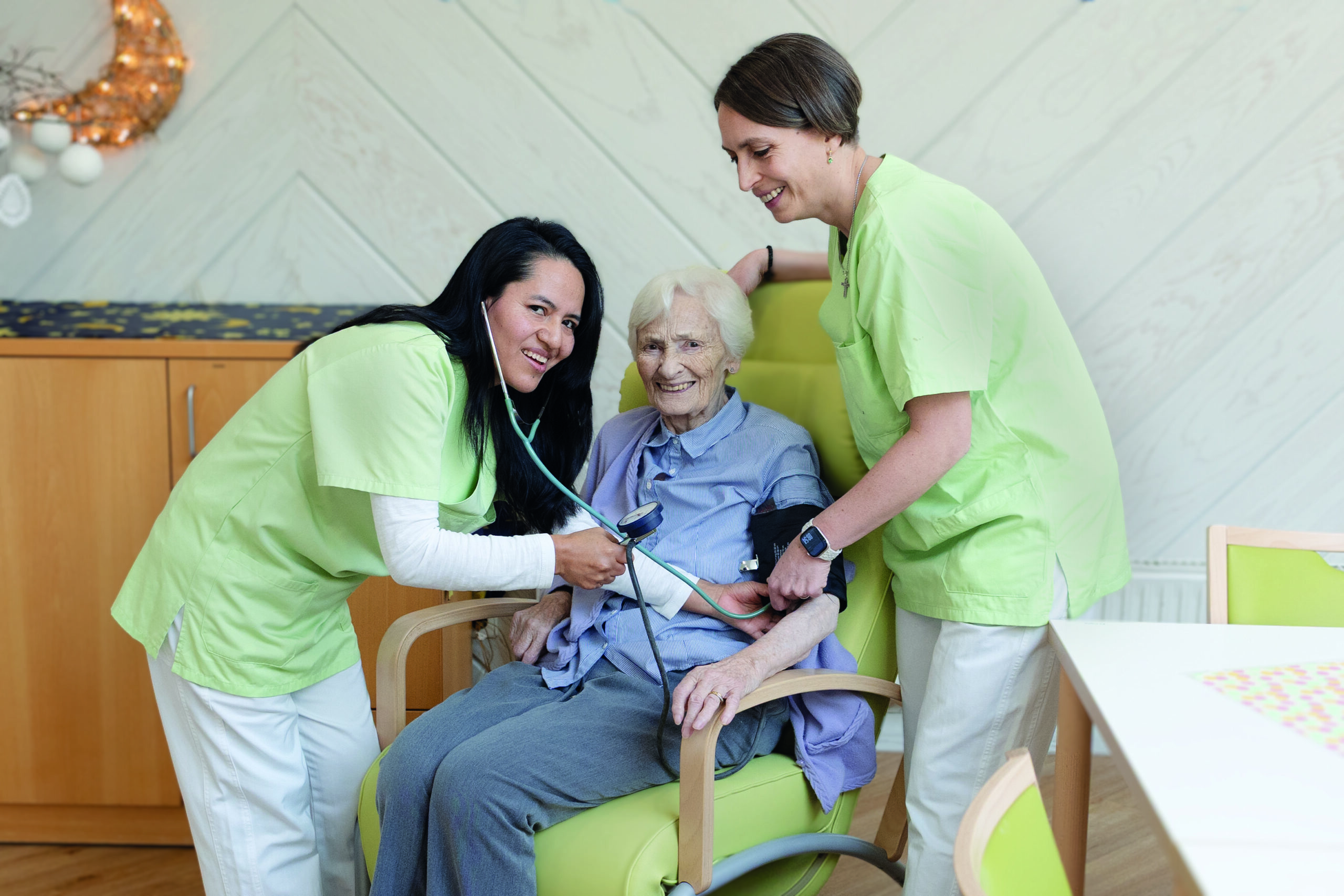 Pflegekräfte messen Blutdruck bei lächelnder Seniorin.