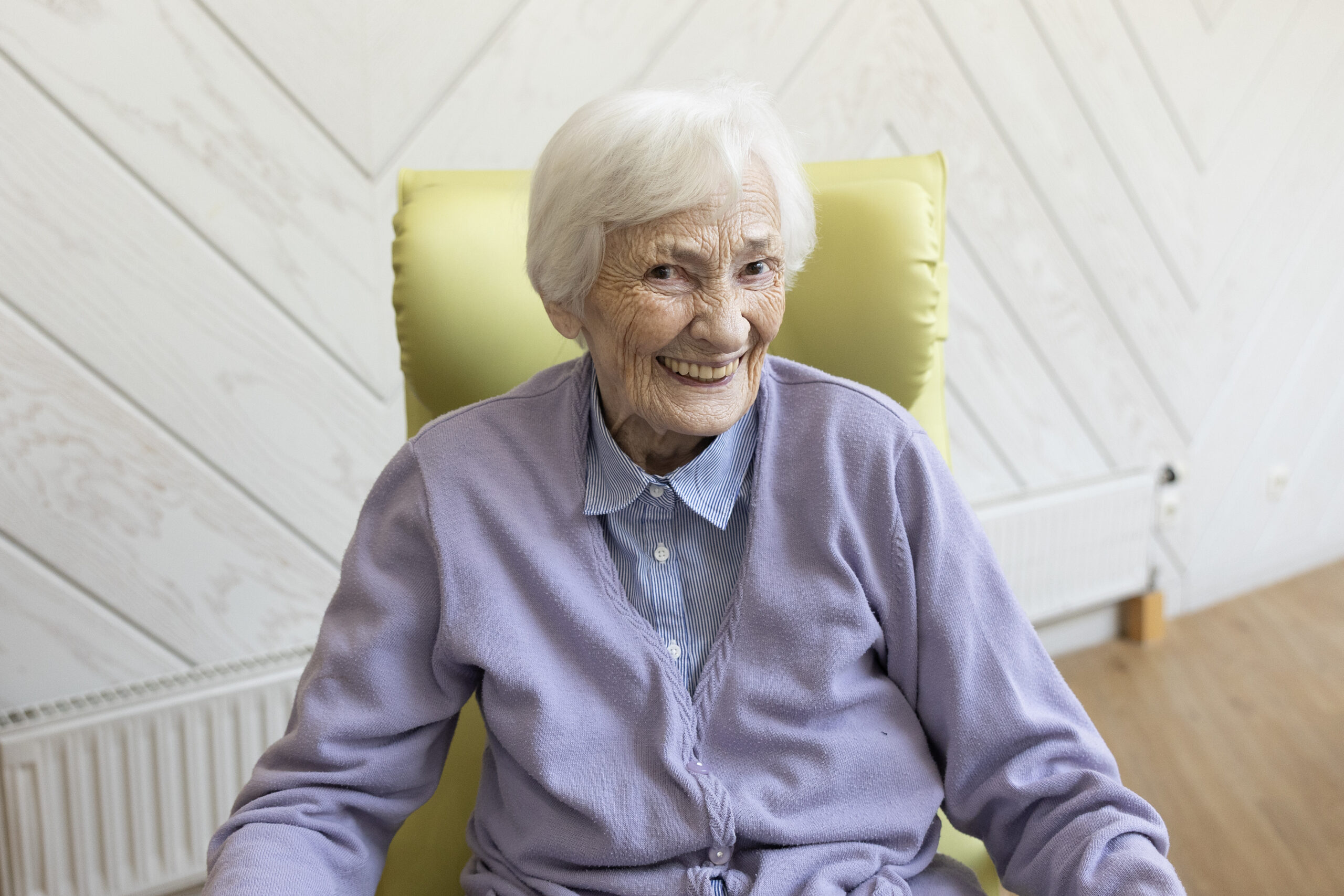 Porträt einer lächelnden Seniorin im hellgrünen Sessel