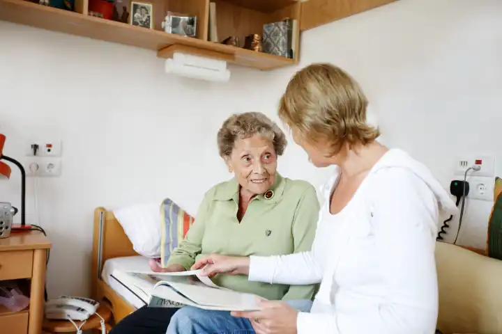 Pflegerin hilft älterer Frau beim Lesen.